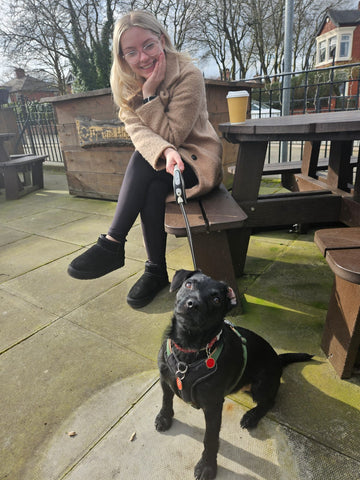 A woman sitting outside with a black dog on a lead.